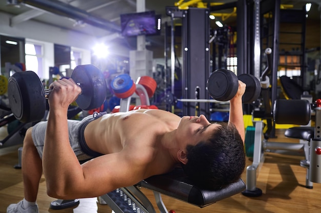 A guy with dumbbells lying doing exercises in the gym