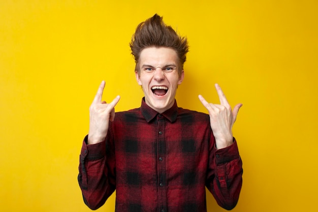 Guy with a funny hairstyle shows a rock sign and screams on a yellow isolated background