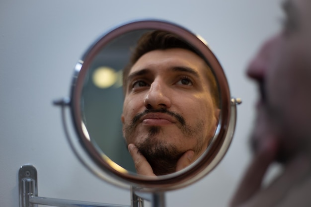 The guy with the rare beard looks in the bathroom mirror in a touched way