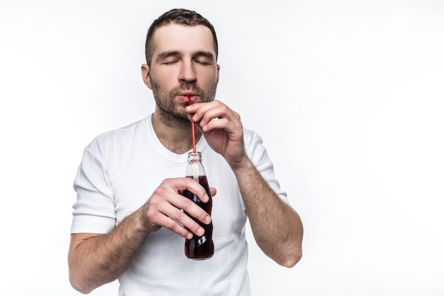 A guy with short cut is drinking coke from the bottle through straw. This man likes to eat fast food and drink sweet drinks. Isolated on white background