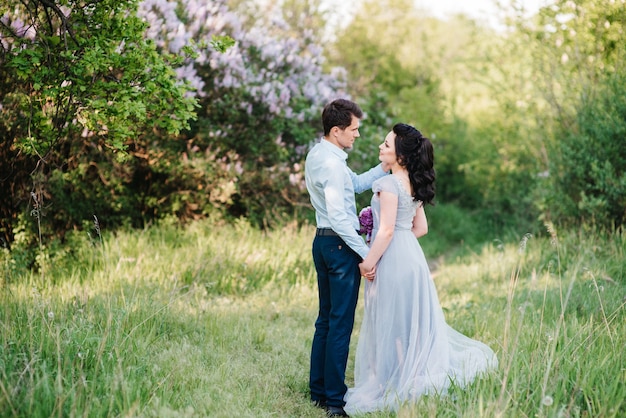 A guy and a woman walk in the spring garden of lilacs before the wedding ceremony