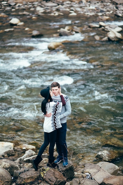 Guy and woman in warm sweaters walking along a mountain river