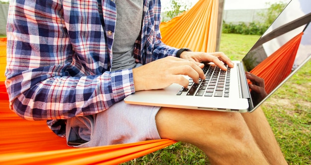 The guy working with laptop online lying in the hammock at the backyard