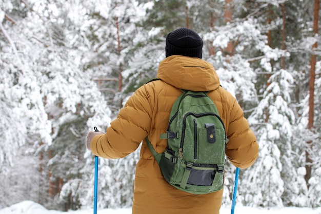 Guy in a yellow down jacket is standing with ski poles or Nordic walking sticks