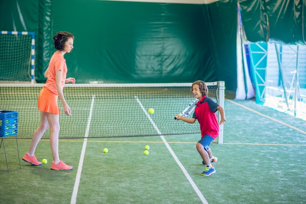 Photo in gym. female coach in bright clothes playing tennis with a boy