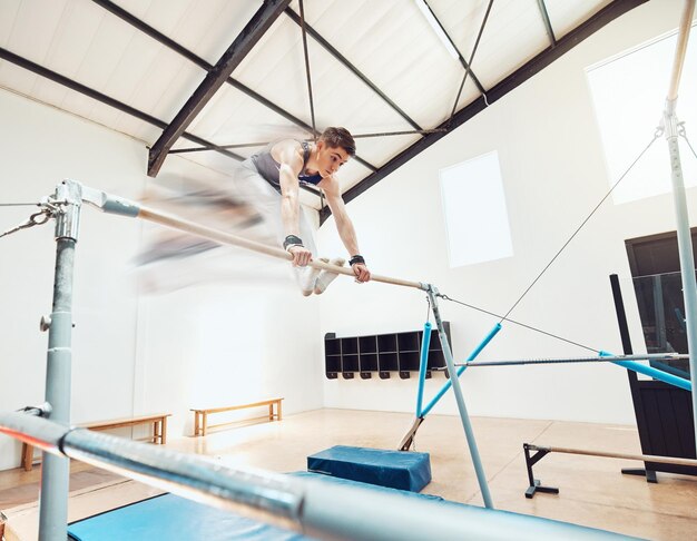 Photo gymnastics olympics and sports with a gymnast swinging on a horizontal bar inside of a gym for fitness training and workout sport exercise and practice with an athlete holding onto parallel bars