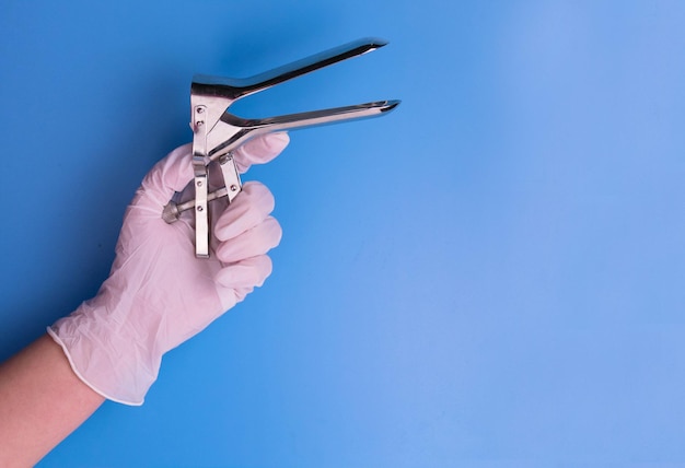 Gynecological mirror in the hand of a doctor on a blue background Medical tool