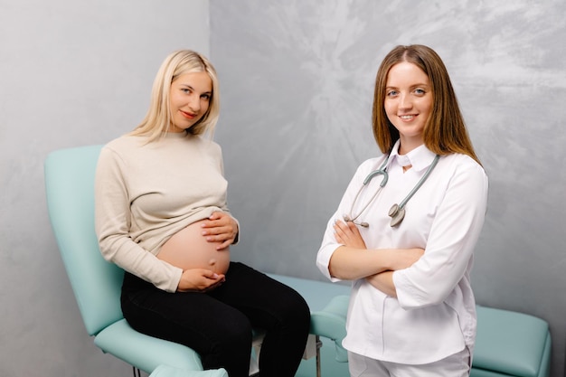 Gynecologist preparing for an examination procedure for a pregnant woman sitting on a gynecological chair in the office and smiling