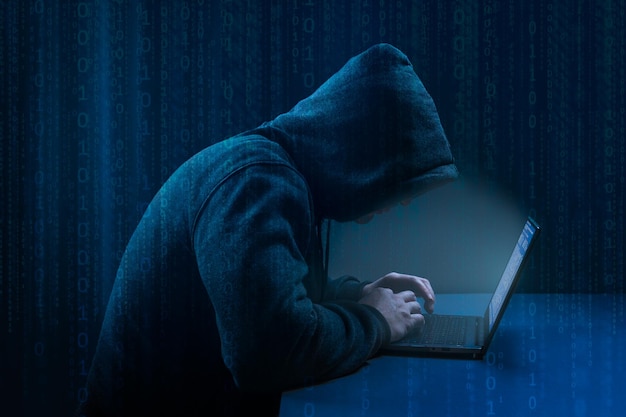 Hacker Hacker using laptop on dark binary code digital background Faceless hooded anonymous computer hacker Hacking and malware concept