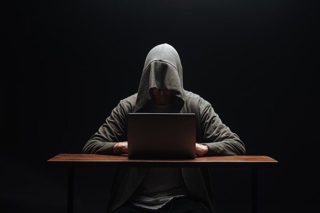 Hacker in a hood with a laptop on a black background