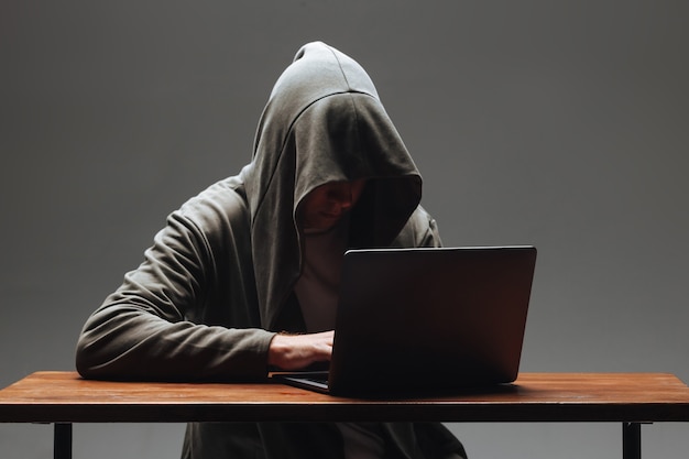 Hacker in a hood without a face sitting at a laptop