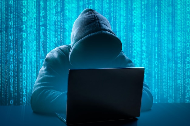 Hacker Using Computer laptop for Organizing Massive Data Breach Attack on Corporate Servers Underground Secret Location Anonymous person in hood sitting in front of computer working with laptop