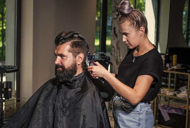 Hair and beard styling brutal guy with barbershop professional master use electric shaver Personal care male barber care bearded man at hairdresser chair in salon beauty and fashion