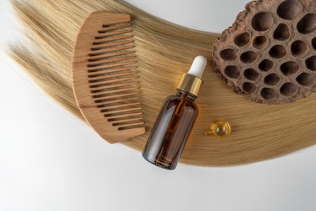 A hair care oil or serum in a brown dropper bottle and golden capsules lying on a blond hair strand product marketing mockup