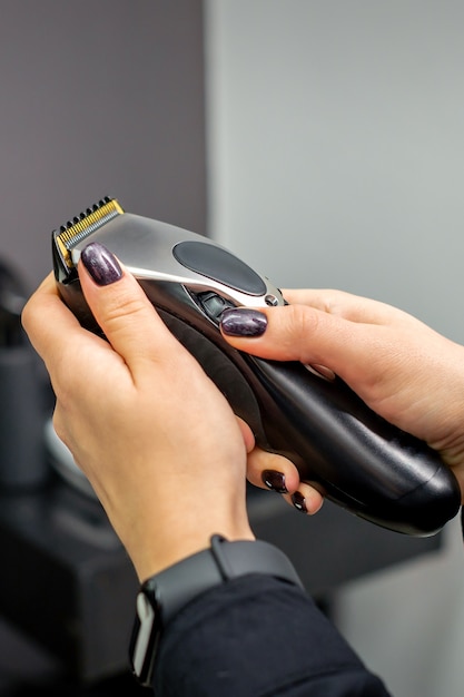 Hair clipper in hands of female professional hairdresser or barber in hair salon