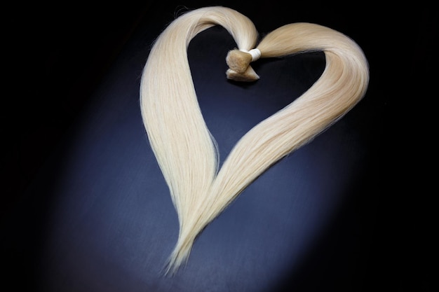 Hair extension equipment of natural blonde hair heart shape on a dark background