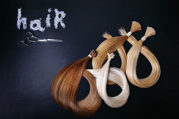 Hair extensions of four colors on a dark background with scissors copyspace top view