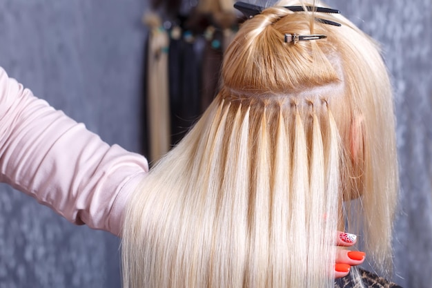 Hair extensions procedure hairdresser does hair extensions to young girl blonde in a beauty salon se