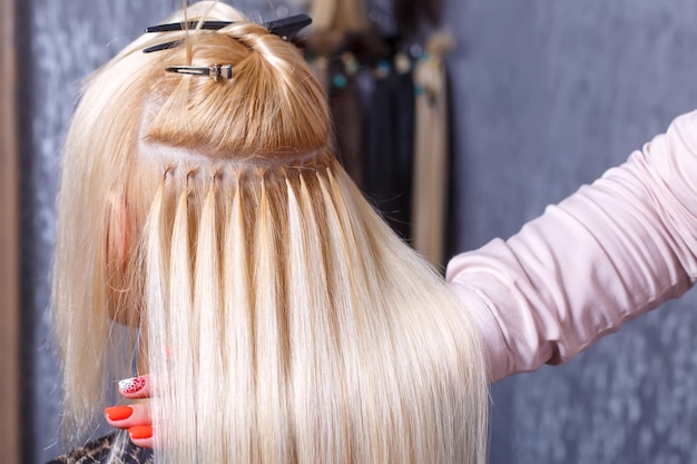 Hair extensions procedure hairdresser does hair extensions to young girl blonde in a beauty salon se