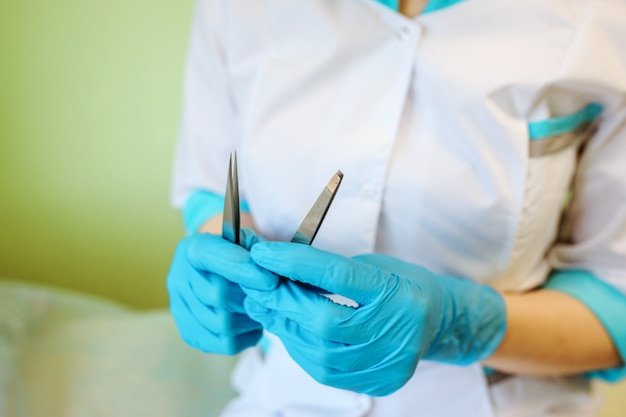 Hair removal instruments, tweezers in the doctor's hands. Doctor is wearing gloves.