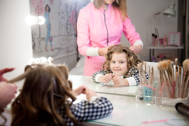 Hair stylist prepares baby girl makes curls hairstyle with curling iron long light brown natural hai