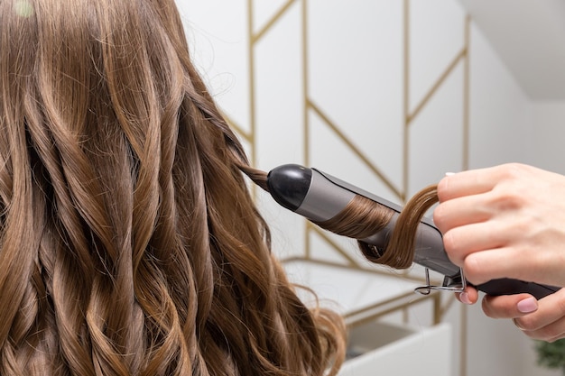 Hair stylist prepares woman makes curls hairstyle with curling iron