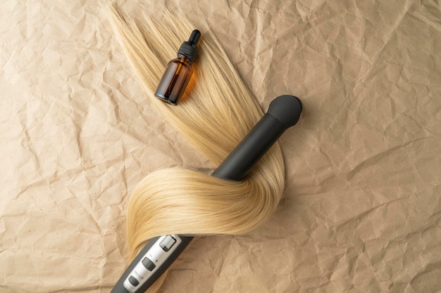 A hair treatment essential oil for smoothing hair and a hair curling styler lying on a brown craft paper background