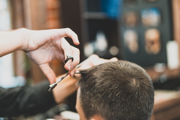 Haircut at the hairdresser. Barber cuts the hair on the client's head. The process of creating hairstyles for men. A man in a barbershop. The near plan. Equipment stylist. Selective focus