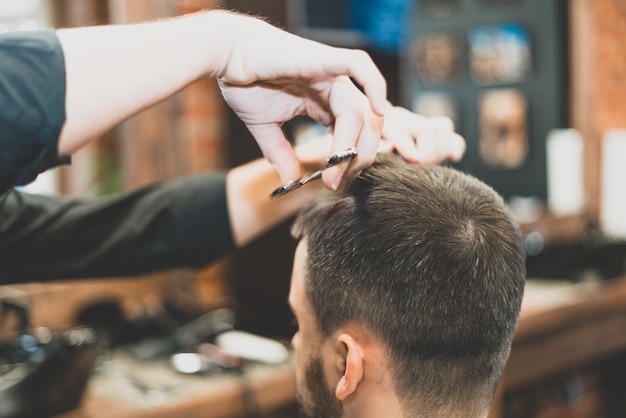 Haircut at the hairdresser. Barber cuts the hair on the client's head. The process of creating hairstyles for men. A man in a barbershop. The near plan. Equipment stylist. Selective focus