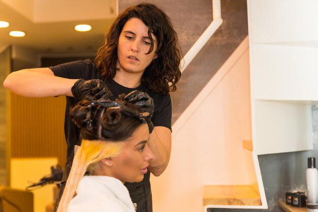 A hairdresser applying a blonde hair dye to a brunette woman while at the beauty salon