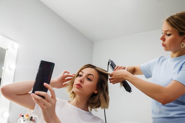 Hairdresser does hairstyle cute pretty young woman in beauty salon. Customer service in interior salon create an amazing image