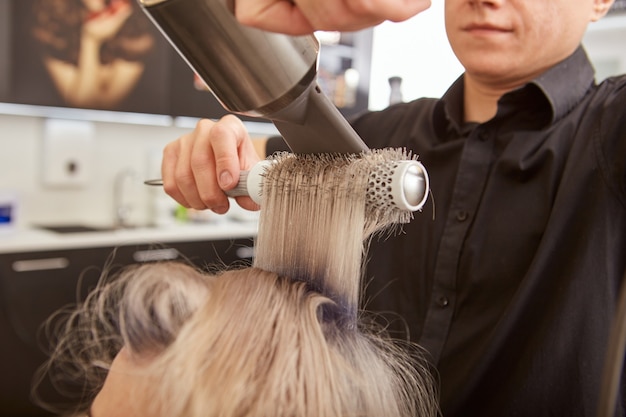 Hairdresser doing blowout hairstyle for client in beauty salon