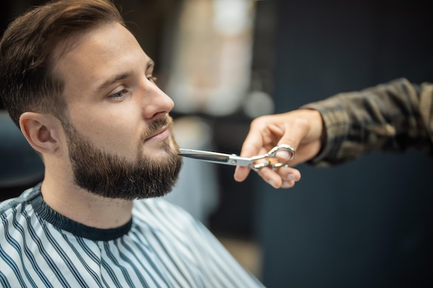 Hairdresser doing haircut of beard using comb and scissors