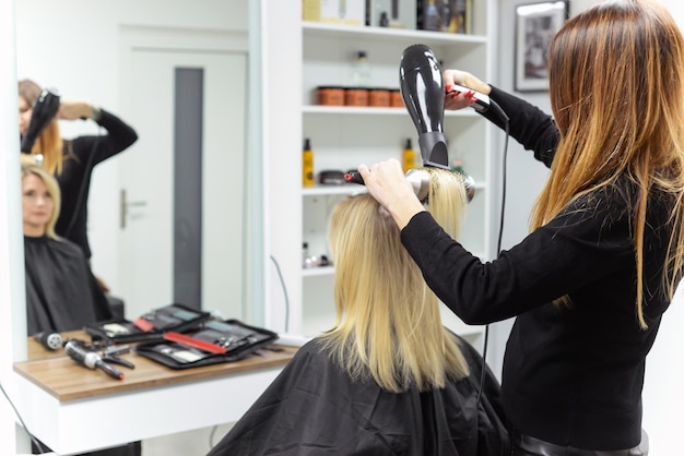 hairdresser dries hair with a hairdryer to a woman after a haircut in the salon