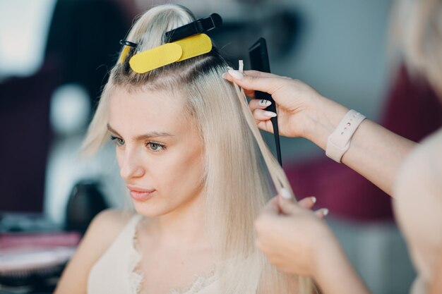 Hairdresser female making hair extensions to young woman with blonde hair in beauty salon Professional hair extension