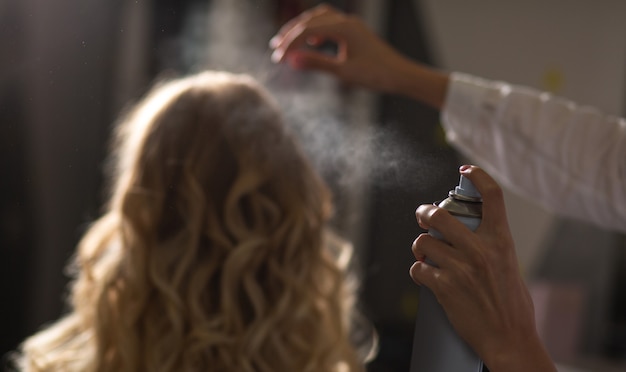 Hairdresser fixing woman's curls with spray at the beauty salon