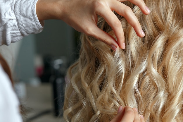 Hairdresser hands touching beautiful client's curls after styling in a beauty salon. Closeup shot