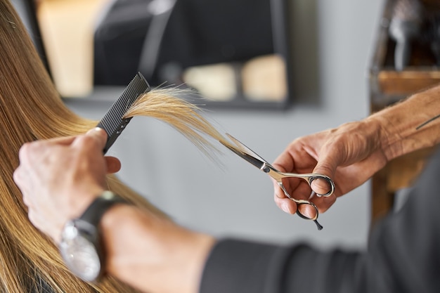 Hairdresser is choping hair of blonde woman is salon