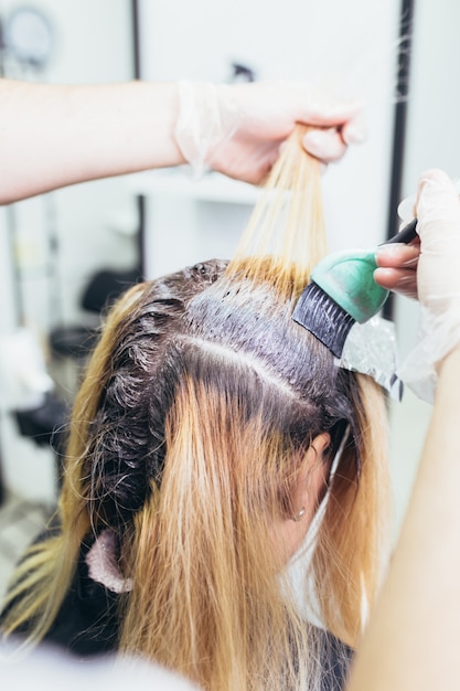 Photo hairdresser is dying female hair, making hair highlights to his client with a foil. selective focus.