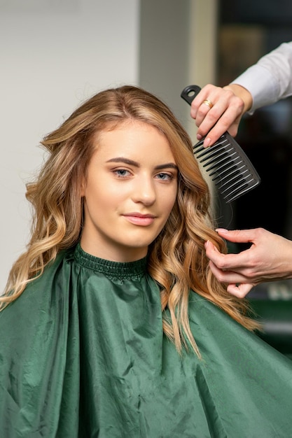 Hairdresser making hairstyling for the woman while combing with hairbrush, comb in a hair salon.