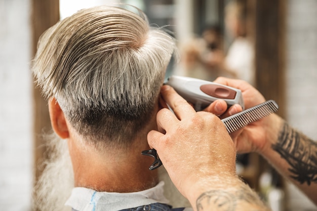 Hairdresser making stylish haircut for  old man in the barbershop