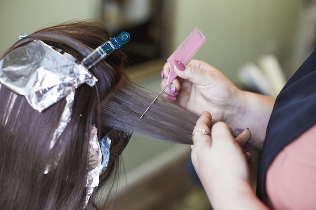 The hairdresser paints a brunette woman's hair in the beauty salon