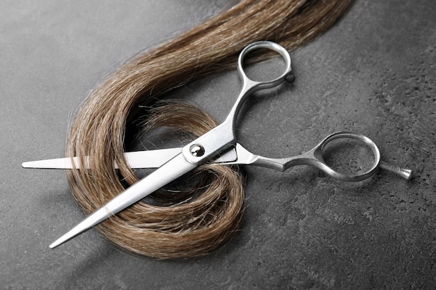 Hairdresser's scissors with strand of brown hair on grey background