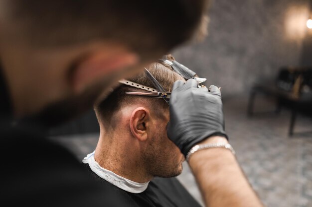 Hairdresser scissors hair on the head sides for a stylish blackhaired man in the barbershop