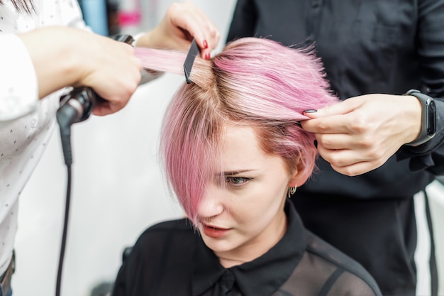 Hairdresser straightening pink hair with hair irons.