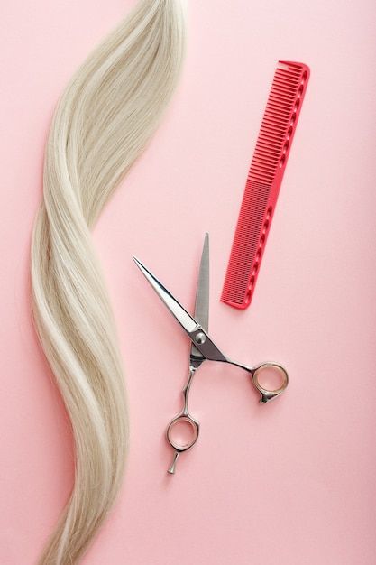 Hairdresser tools scissors, combs and strand of blonde hair on pink color background Beauty salon service