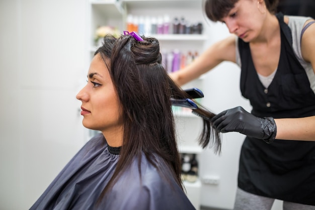 Hairdresser using a hair straightened to straighten the hair Hair stylist working on a woman's hair style at salonHair care Beautiful attractive woman in a beauty salon