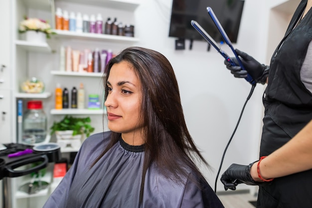 Hairdresser using a hair straightened to straighten the hair Hair stylist working on a woman's hair style at salonHair care Beautiful attractive woman in a beauty salon