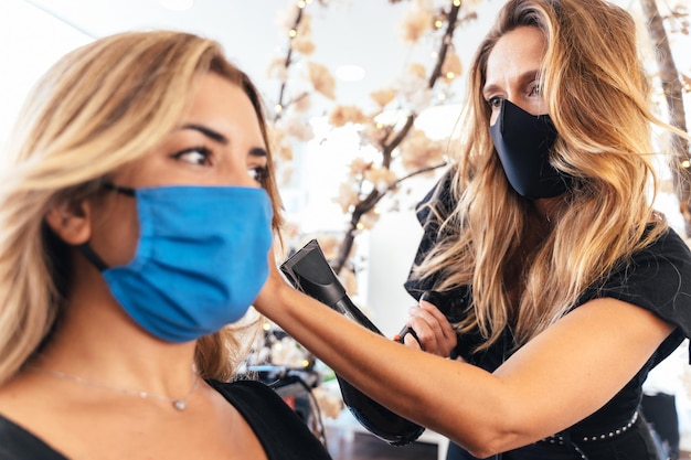 Hairdresser with facial mask drying the hair of a client