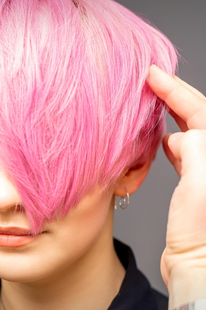 Hairdresser with hands and comb is checking out and fixing the short pink hairstyle of the young white woman in a hair salon